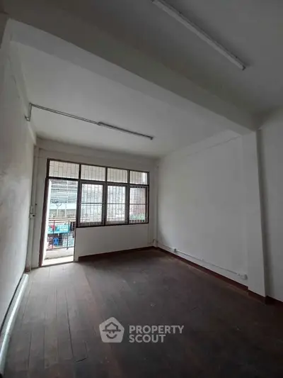 Spacious empty room with large window and wooden flooring, ideal for customization.