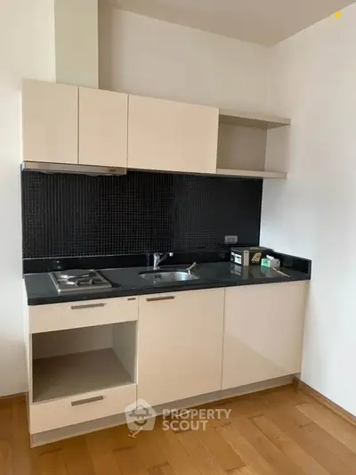 Modern compact kitchen with sleek cabinetry and black backsplash in a cozy apartment.