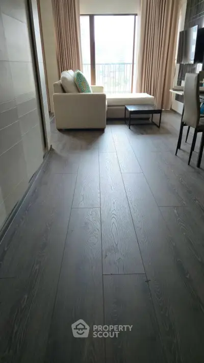Spacious living room with elegant wooden flooring and modern furniture, featuring a large window with city view.