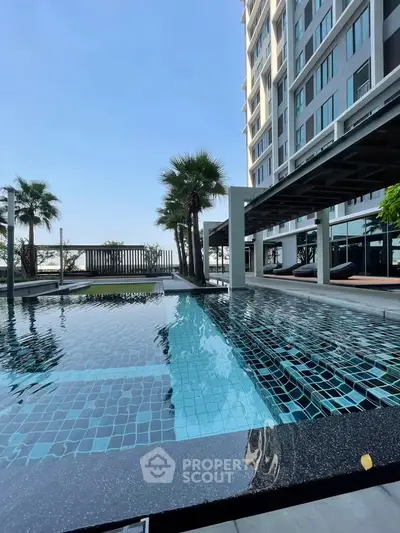Luxurious poolside view at modern high-rise building with palm trees and clear blue sky.