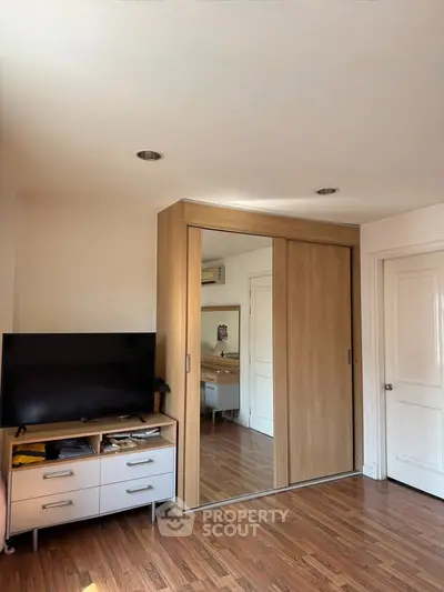 Spacious bedroom with mirrored wardrobe and sleek TV stand, featuring elegant wooden flooring.