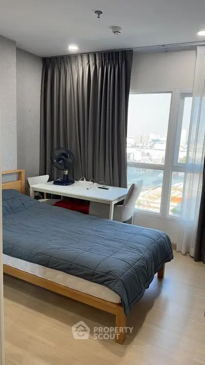 Modern bedroom with city view, featuring a cozy bed and work desk by the window.