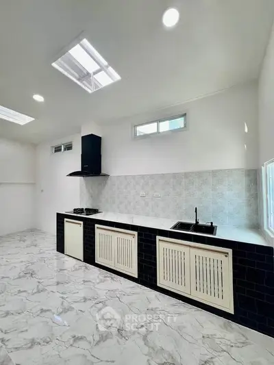 Modern kitchen with sleek black and white design, featuring gas stove and ample natural light.