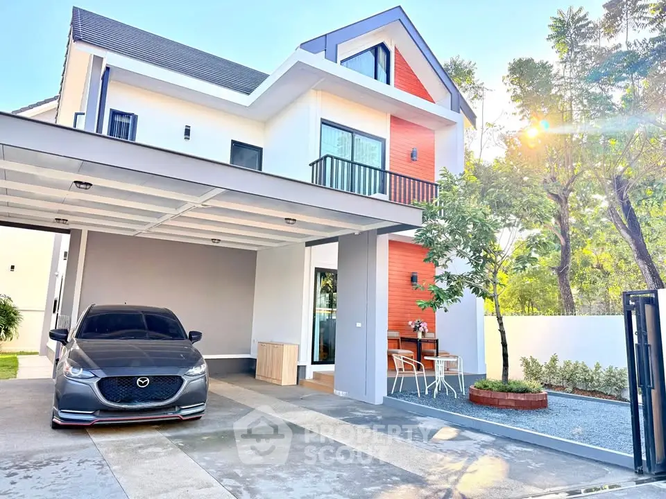 Modern two-story house with carport and outdoor seating area, surrounded by lush greenery.