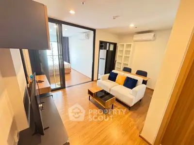 Modern living room with wooden flooring, stylish furniture, and a view into a cozy bedroom.