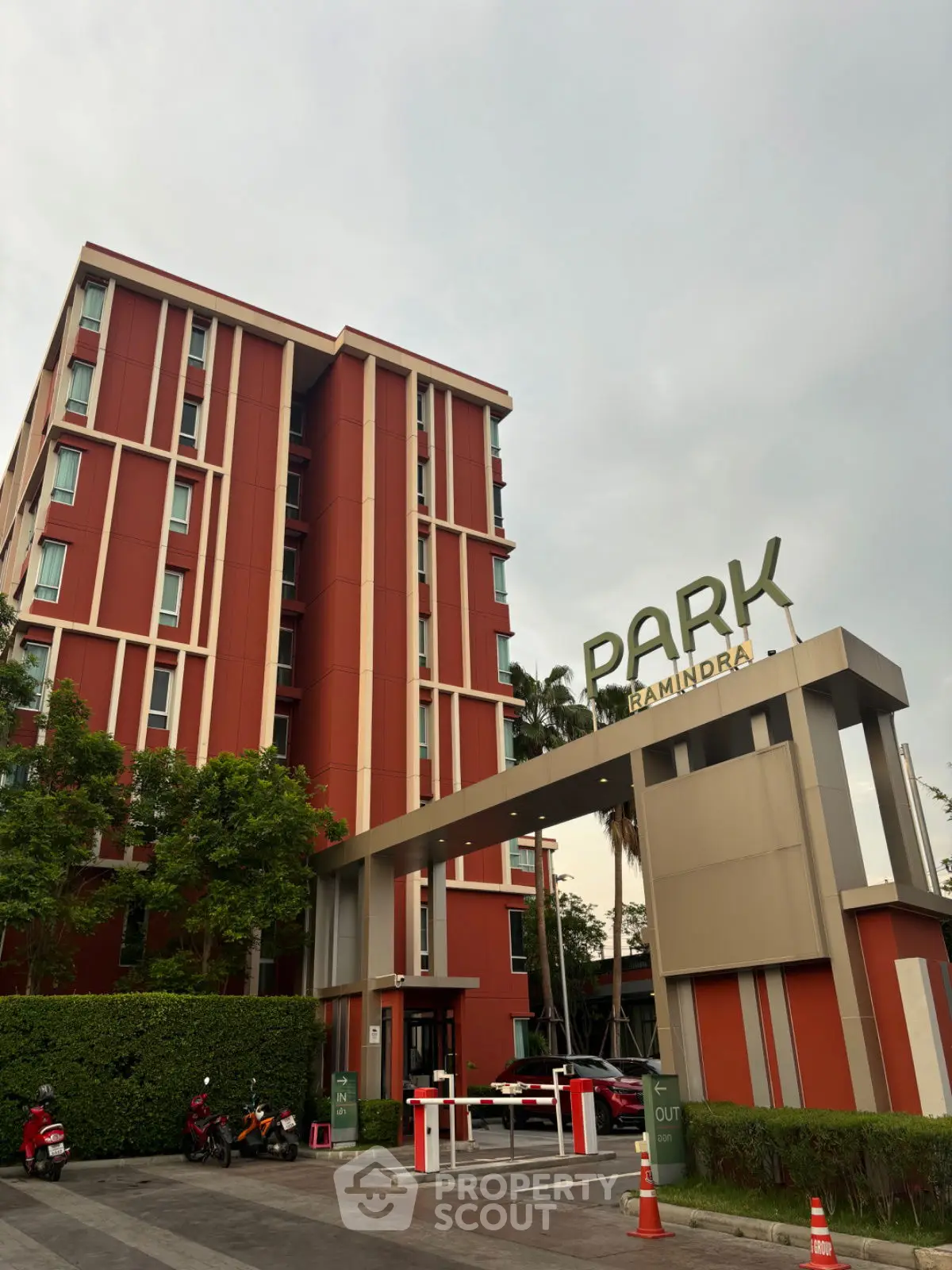Modern apartment building with striking red facade and lush greenery at entrance.