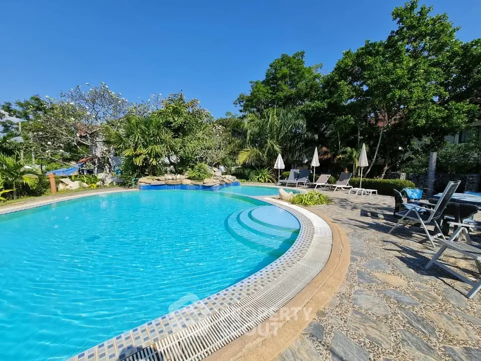 Luxurious outdoor pool area with lush greenery and sun loungers, perfect for relaxation and leisure.