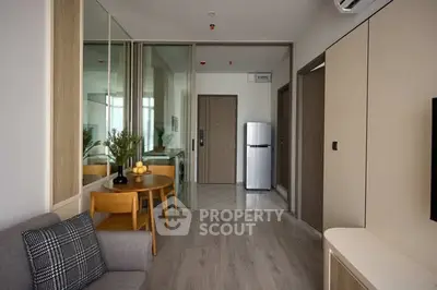 Modern apartment interior with sleek design, featuring a cozy living area and compact kitchen with stainless steel fridge.