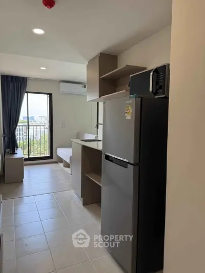 Modern apartment kitchen with fridge and open layout, featuring natural light and city view.