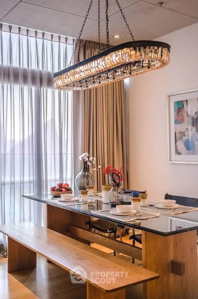 Elegant dining room with glass table, wooden benches, and modern chandelier in a stylish apartment.