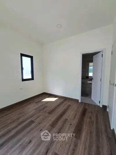 Spacious empty room with wooden flooring and bathroom access