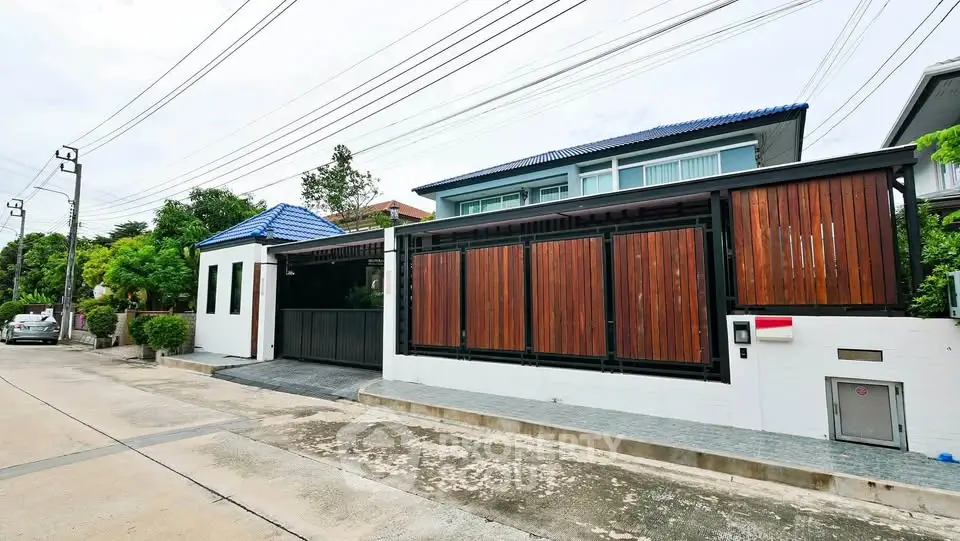 Modern house exterior with wooden gate and blue roof in suburban neighborhood