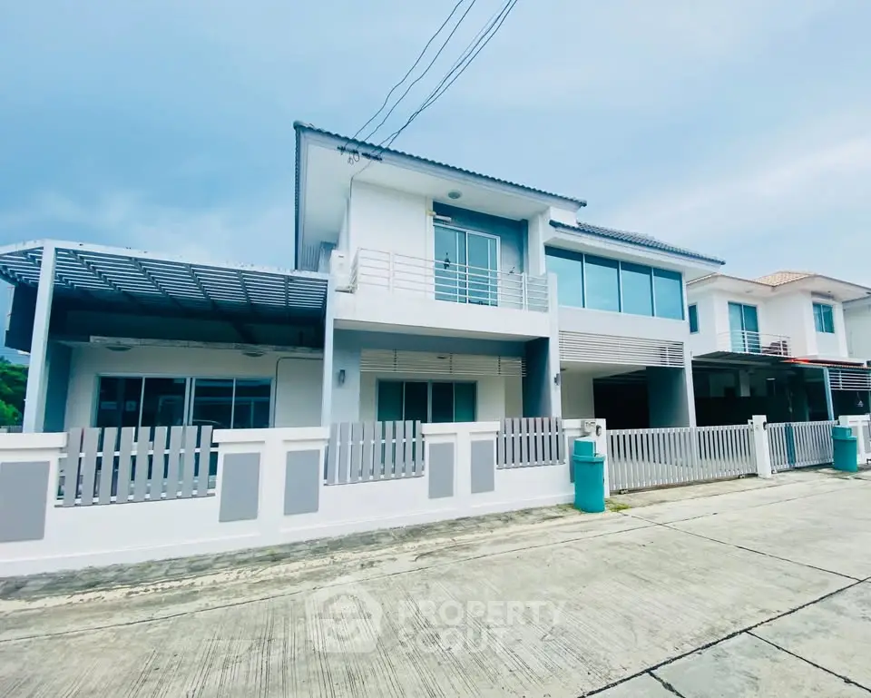 Modern two-story house with large windows and balcony in a serene neighborhood.
