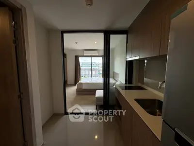 Modern apartment with sleek kitchen and cozy bedroom, featuring a glass partition for an open feel.