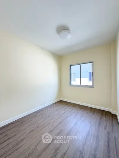 Spacious empty room with wooden flooring and natural light from window