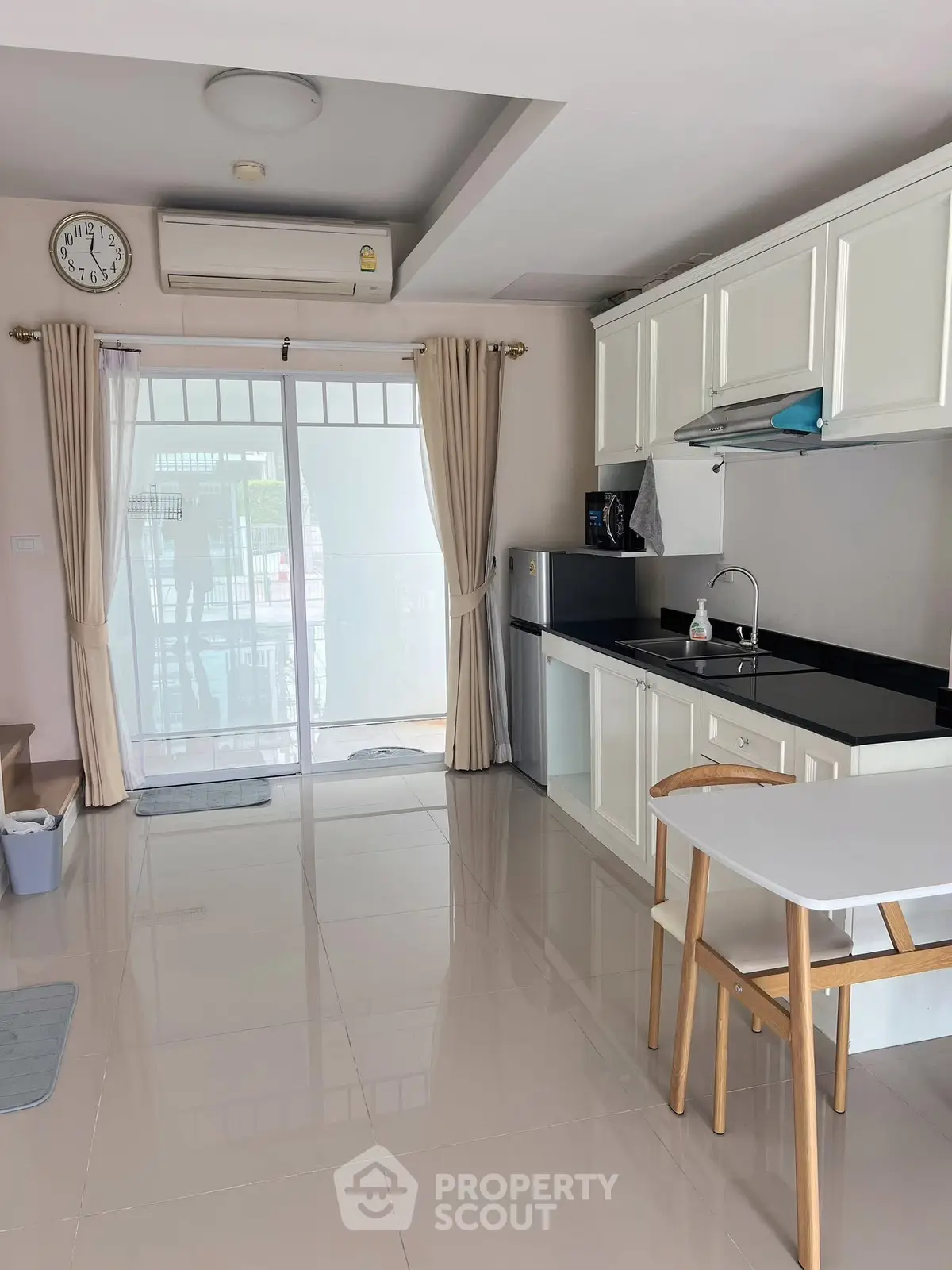 Modern kitchen with sleek white cabinets and dining area, featuring a large window for natural light.