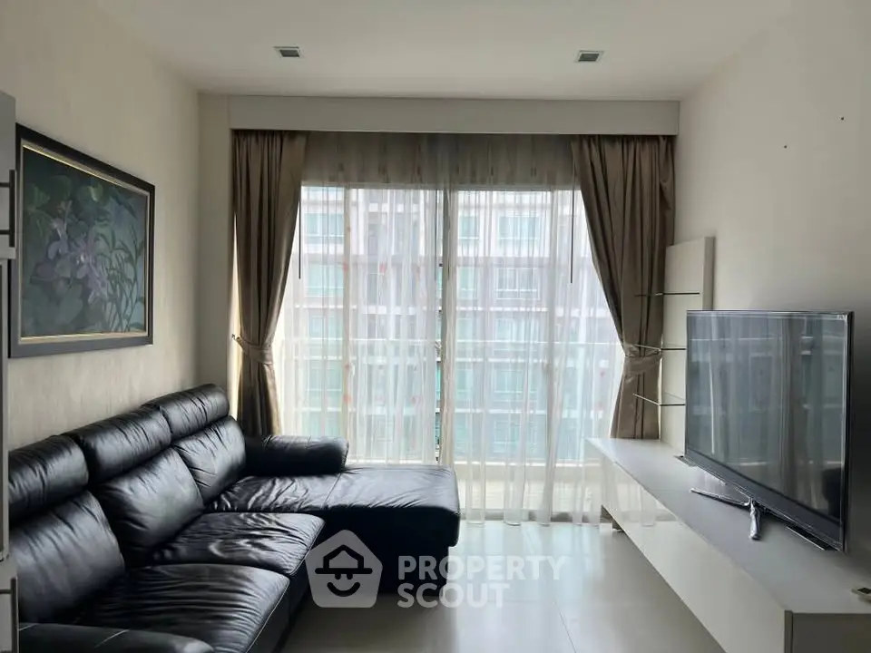 Modern living room with black leather sofa and large TV, featuring floor-to-ceiling windows with city view.