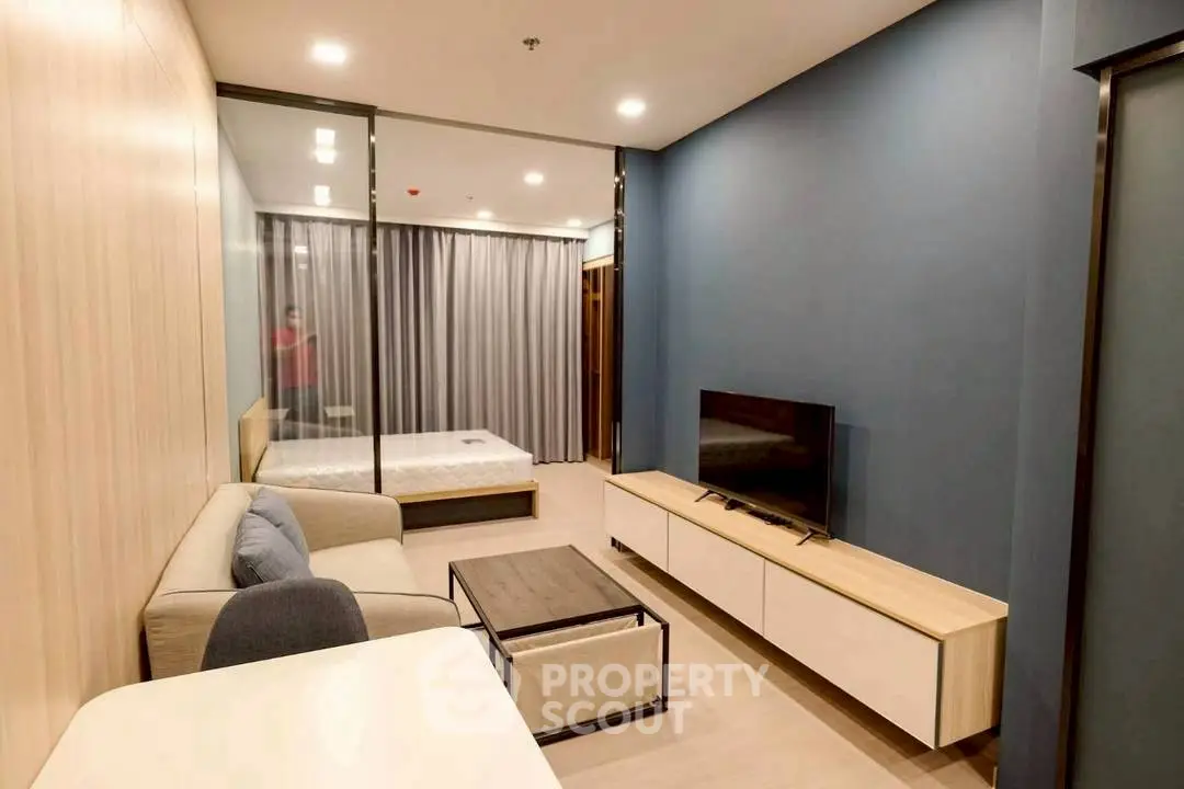 Modern studio apartment with stylish living area and cozy bedroom separated by glass partition.
