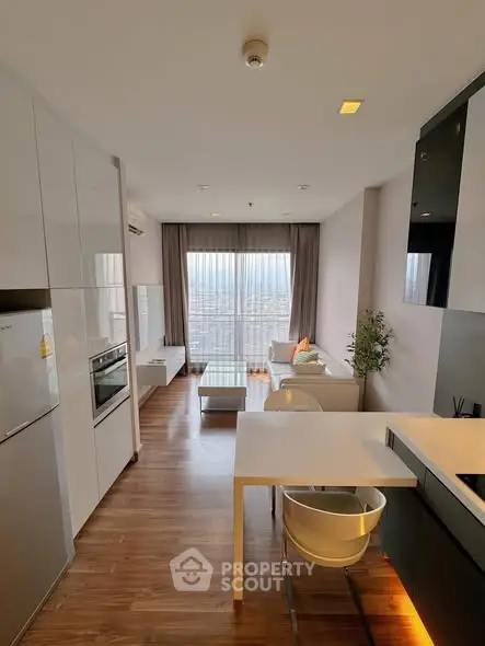 Modern open-plan living room with kitchen, featuring sleek furniture and large windows with city views.