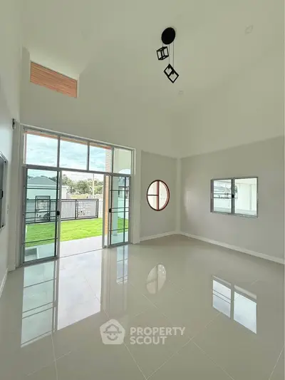 Spacious modern living room with high ceilings and large windows opening to a lush garden view.
