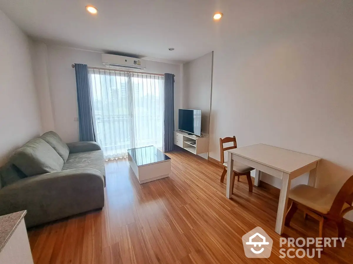 Spacious living room with polished wooden flooring, comfortable sofa, and ample natural light filtering through sheer curtains, perfect for urban living.