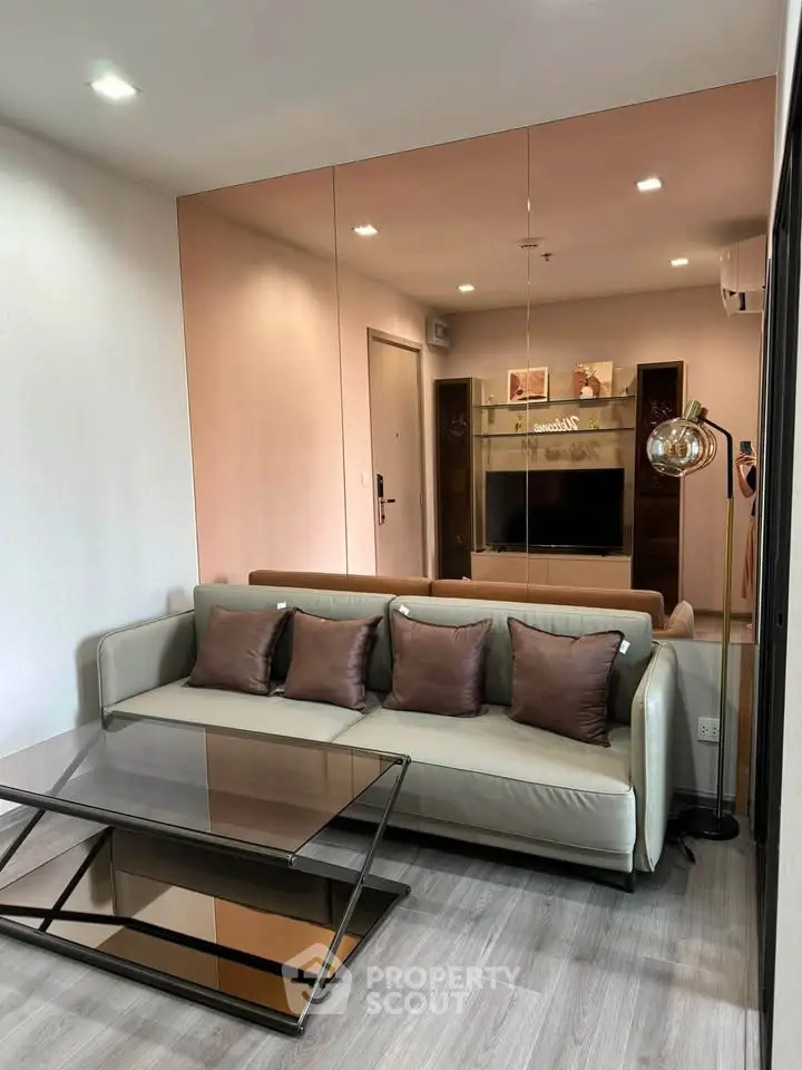 Modern living room with stylish sofa, glass coffee table, and mirrored wall enhancing space.