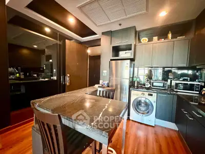 Modern kitchen with marble island, washing machine, and sleek dark cabinetry in a stylish apartment.