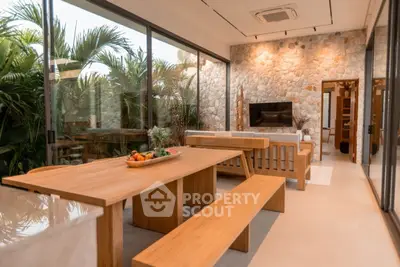 Luxurious open-plan living area with stone wall and garden view, featuring elegant wooden furniture.