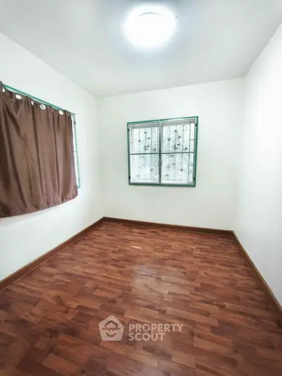 Spacious empty room with wooden flooring and natural light from windows.