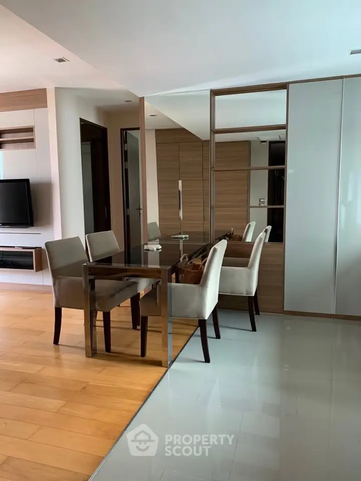 Modern dining area with sleek glass table and stylish chairs in open-plan living space.