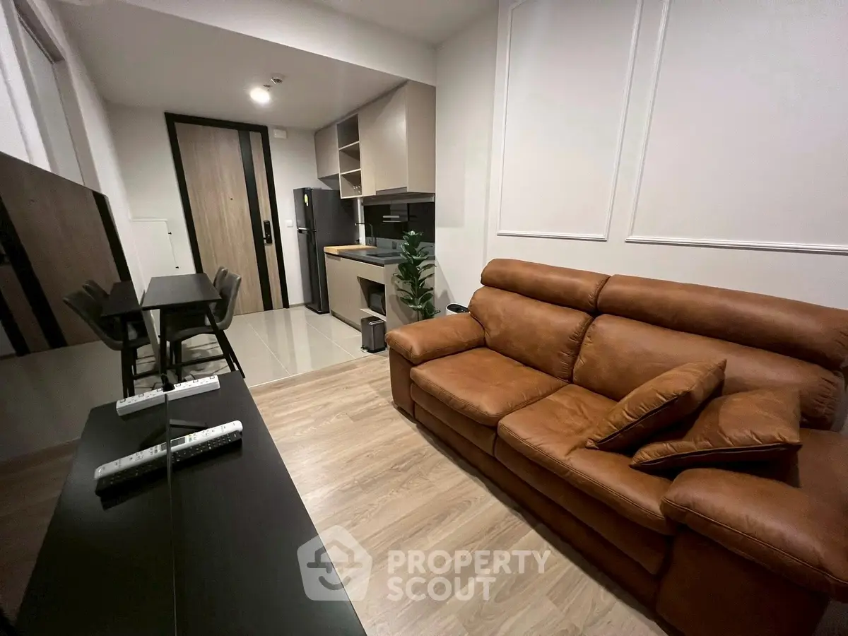 Modern living room with brown leather sofa and sleek kitchen area in open layout apartment.