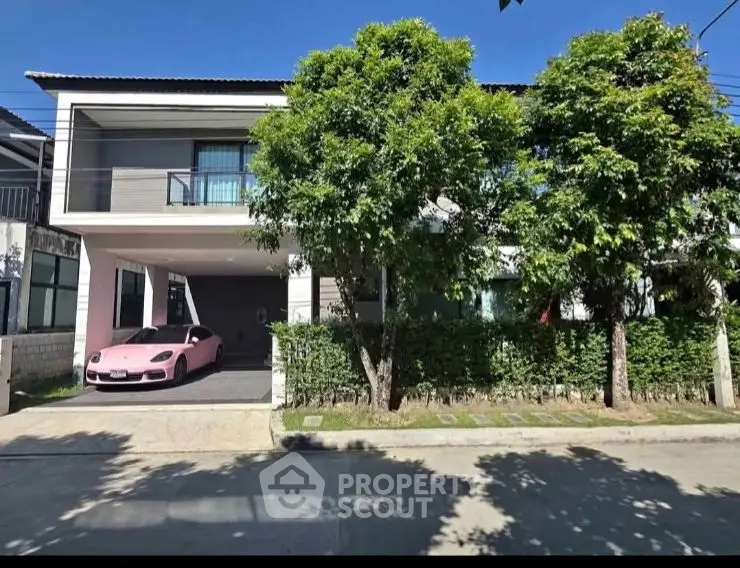 Modern house exterior with driveway and car, surrounded by lush greenery.