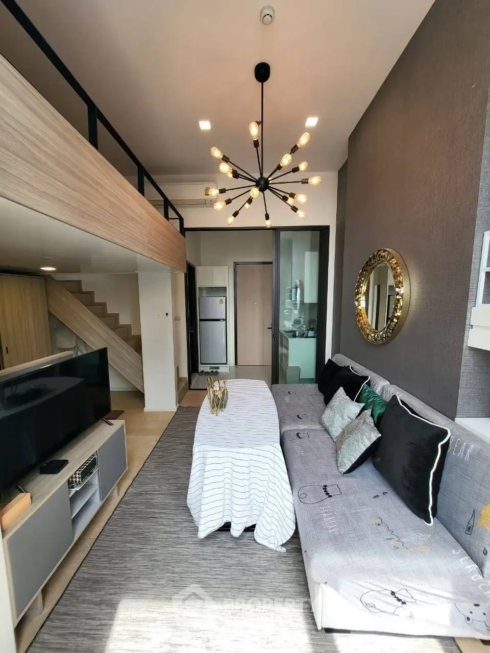 Modern living room with loft, stylish chandelier, and cozy sofa in a bright apartment.