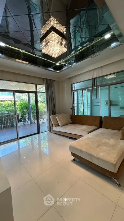 Spacious living room with modern chandelier and large windows opening to a garden view.