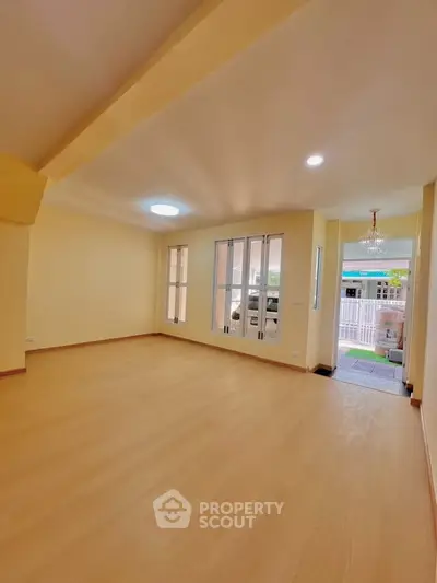 Spacious living room with large windows and wooden flooring, perfect for natural light and comfort.