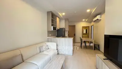 Modern living room with open kitchen and dining area, featuring sleek furniture and neutral tones.