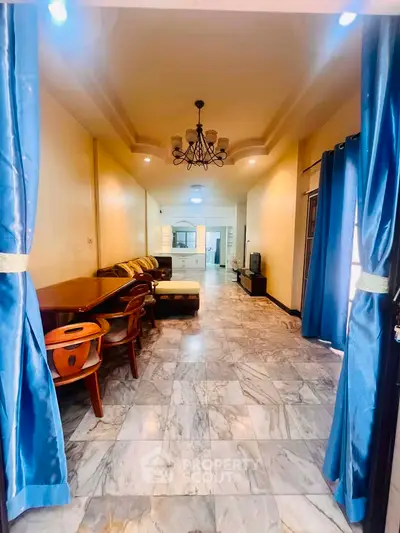 Spacious living room with elegant chandelier and marble flooring, featuring a cozy seating area and dining space.