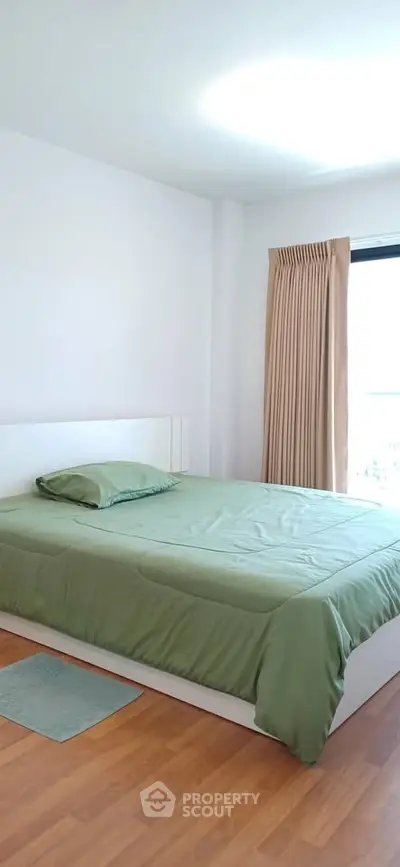 Bright and cozy bedroom with green bedding and wooden flooring, perfect for relaxation.
