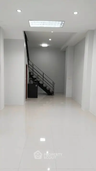 Spacious modern interior with sleek staircase and glossy white flooring, perfect for versatile living or office space.