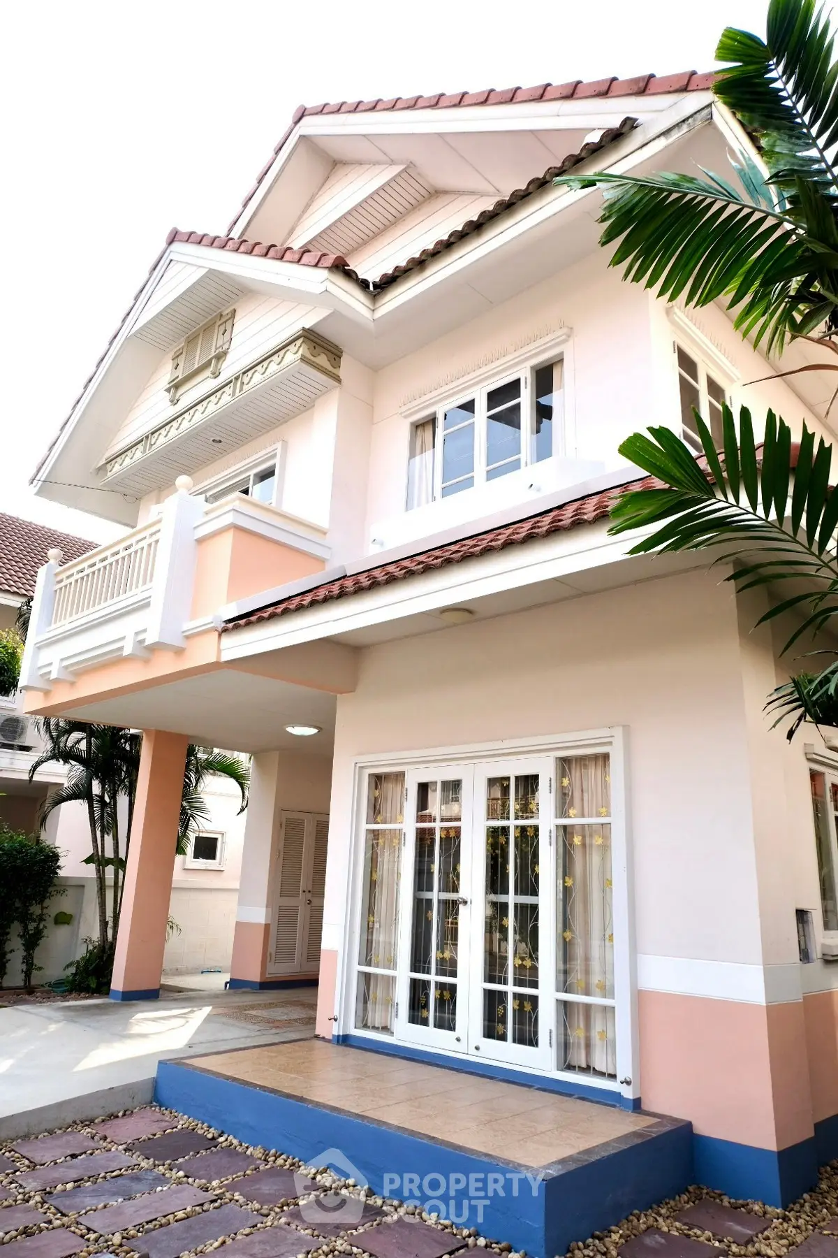 Charming two-story house with elegant balcony and lush palm trees, perfect for family living.