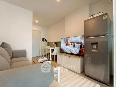 Modern living room with cozy sofa, flat-screen TV, and sleek refrigerator in open layout.