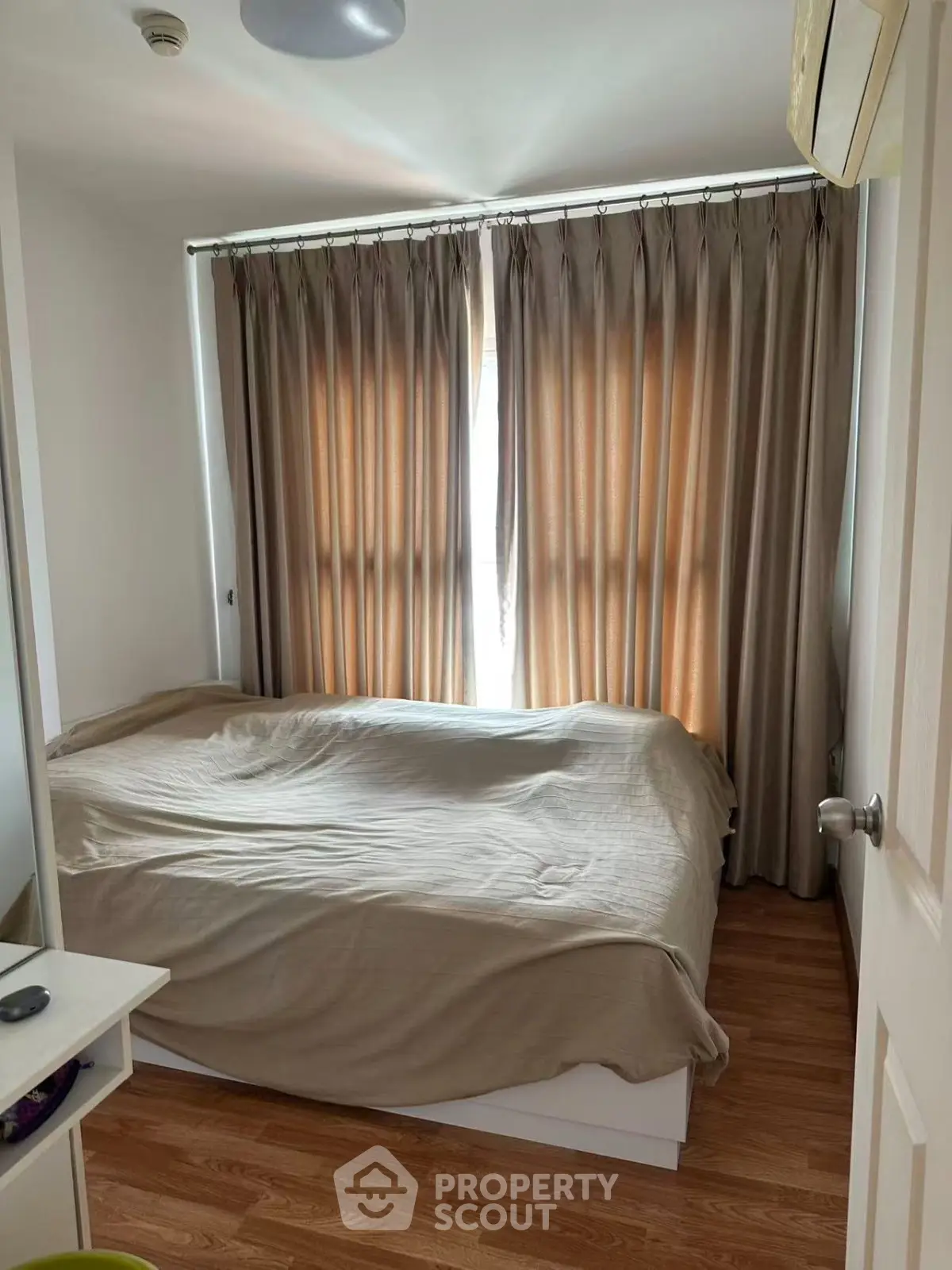Cozy bedroom with wooden flooring and large window draped with curtains, perfect for restful nights.