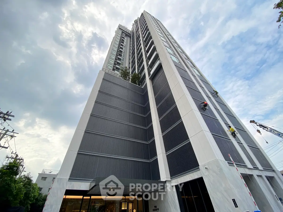 Modern high-rise building with sleek design and glass facade under a cloudy sky.