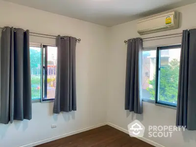 Bright bedroom with dual windows and air conditioning unit, featuring modern gray curtains and wooden flooring.