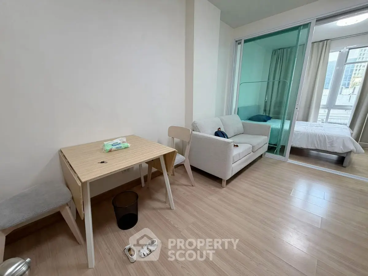 Modern studio apartment with cozy living area and bedroom separated by glass partition, featuring minimalist furniture.