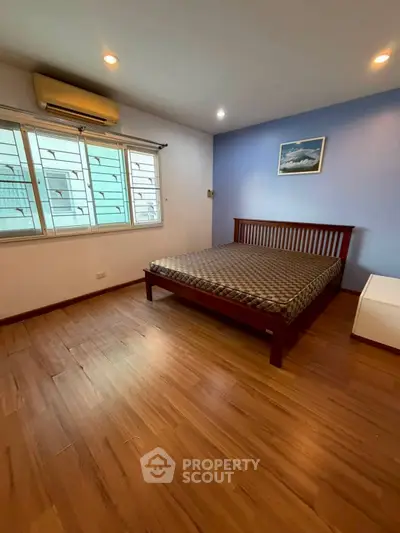Spacious bedroom with wooden flooring and large window in modern apartment