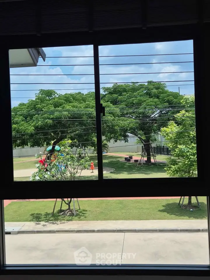 Scenic view from window overlooking lush green garden and playground area.