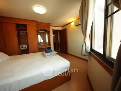 Spacious bedroom with wooden furniture and large window offering natural light.