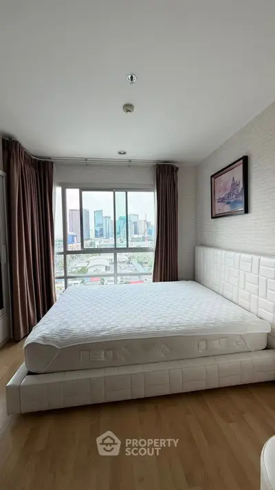 Spacious bedroom with large window offering stunning city skyline view, featuring modern decor and elegant furnishings.