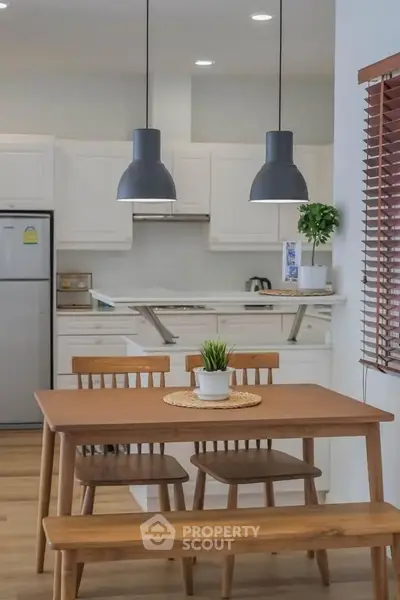 Modern kitchen with wooden dining set and pendant lights, featuring sleek white cabinetry and stainless steel appliances.